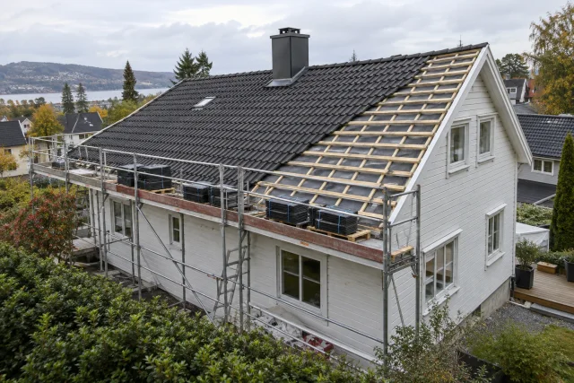 Illustrasjon av takbytte på et hvitt trehus, med stillas, takstein og synlige lekter over undertaket.
