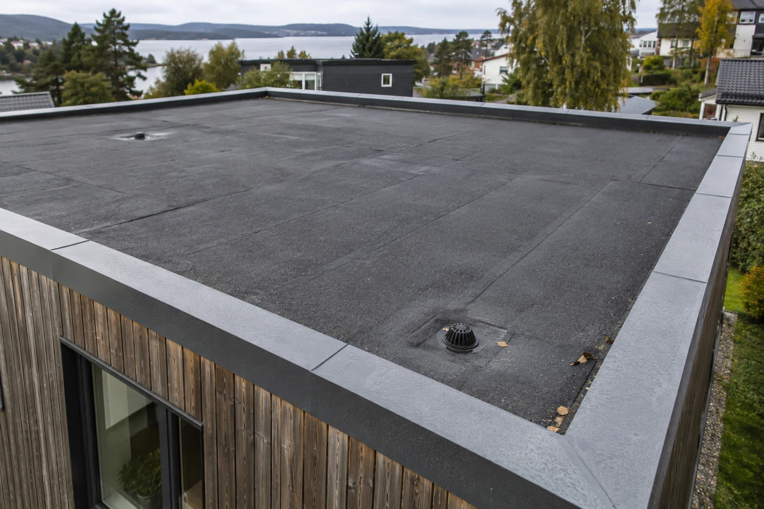 Fotorealistisk illustrasjon av et flatt tak med mørkt takbelegg, to sluk og metallbeslag langs kanten