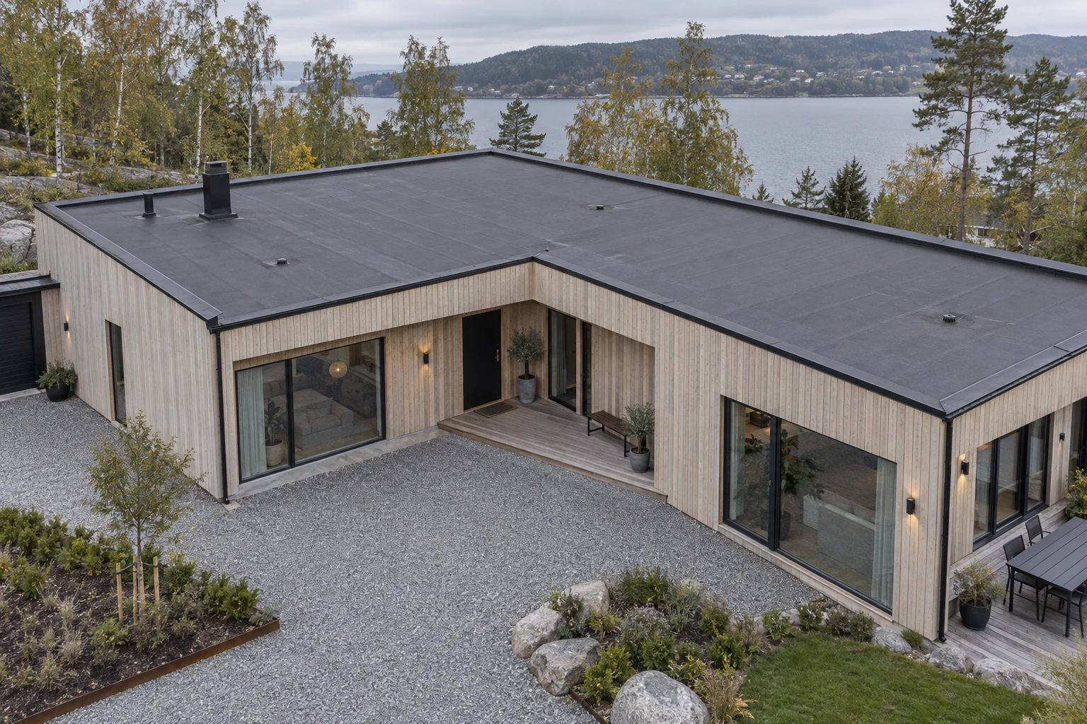 Moderne trehus sett ovenfra med mørkt takbelegg, parapeter og sluk på et flatt tak.