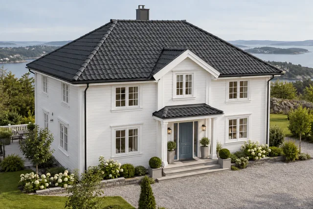 Hvitt trehus med valmtak og mørk takstein, sett fra en vinkel som viser takflatene.